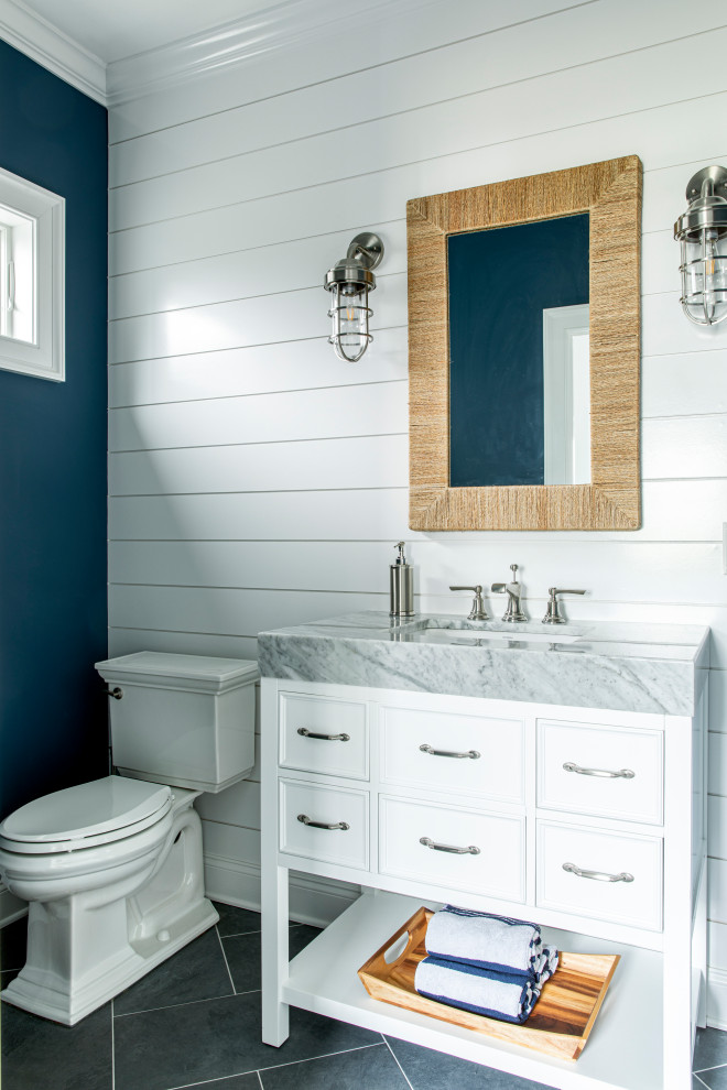 Aménagement d'une salle de bain bord de mer avec des portes de placard blanches, WC séparés, un mur bleu et un lavabo encastré.
