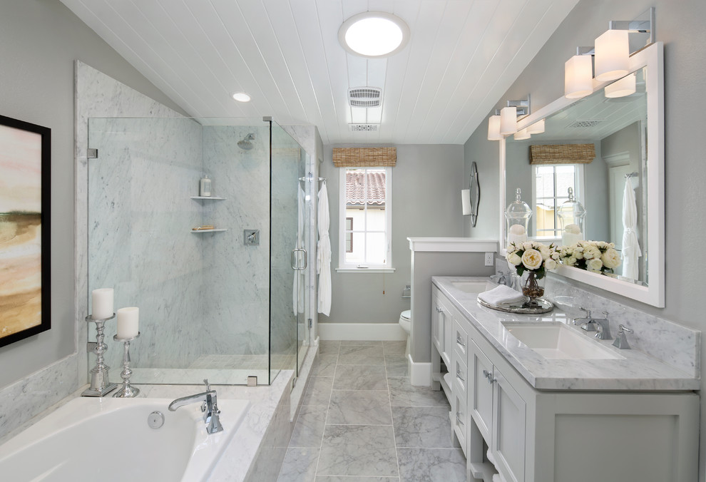 Cette image montre une salle de bain principale et grise et blanche traditionnelle avec un placard avec porte à panneau encastré, des portes de placard grises, une baignoire posée, un carrelage gris, un mur gris, un lavabo encastré et une cabine de douche à porte battante.