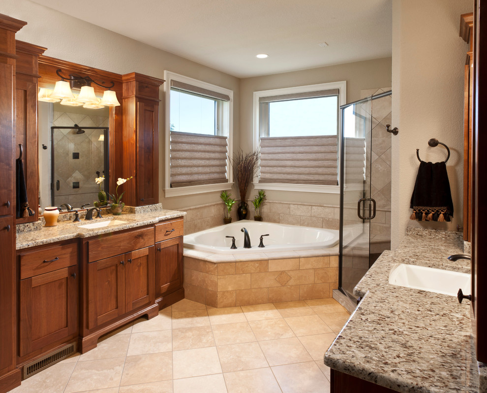 Cette photo montre une salle de bain principale chic en bois brun avec un lavabo intégré, un placard avec porte à panneau encastré, un plan de toilette en granite, une baignoire d'angle, une douche d'angle, un carrelage beige, des carreaux de céramique, un mur beige et un sol en carrelage de céramique.