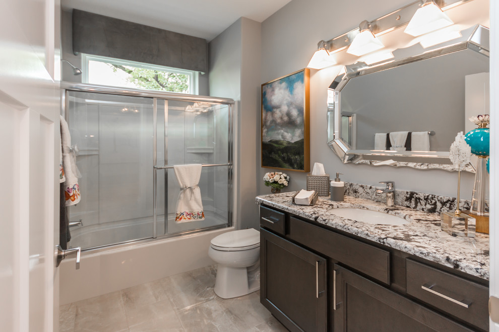 Photo of a medium sized traditional family bathroom in Milwaukee with shaker cabinets, dark wood cabinets, a shower/bath combination, a one-piece toilet, grey walls, porcelain flooring, a submerged sink, granite worktops, a sliding door, white worktops and beige floors.