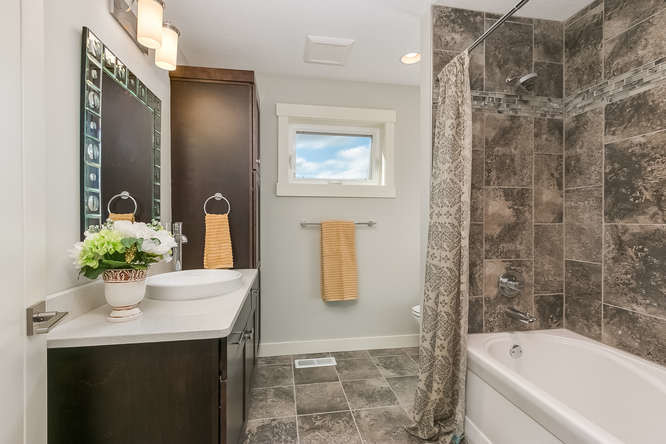 На фото: главная ванная комната среднего размера в современном стиле с накладной раковиной, фасадами с утопленной филенкой, темными деревянными фасадами, ванной в нише, душем над ванной, унитазом-моноблоком и серыми стенами с