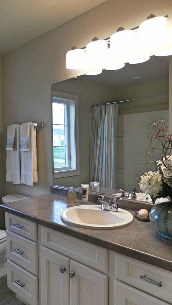 This is an example of a farmhouse bathroom in Other with a built-in sink, recessed-panel cabinets, white cabinets, laminate worktops, an alcove bath, a double shower, a two-piece toilet and grey tiles.