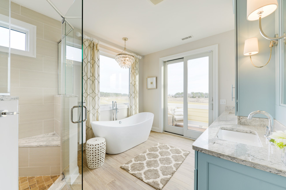 Aménagement d'une salle de bain bord de mer avec un placard avec porte à panneau encastré, des portes de placard bleues, une baignoire indépendante, une douche d'angle, un lavabo encastré et un sol gris.