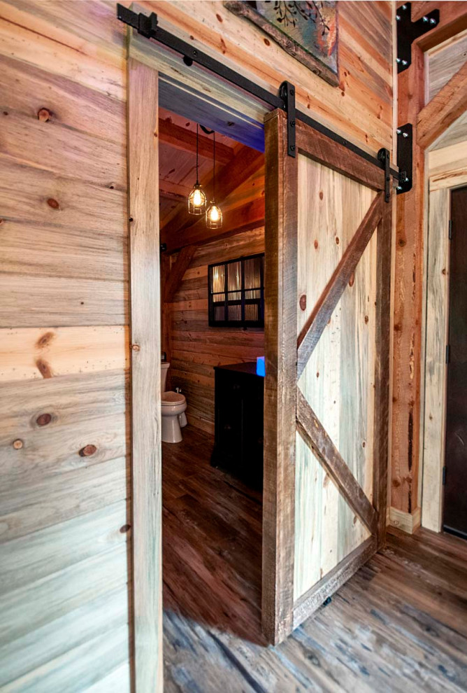 Modelo de cuarto de baño principal y único rústico de tamaño medio con puertas de armario negras, sanitario de una pieza, suelo de madera en tonos medios, cuarto de baño, machihembrado y machihembrado