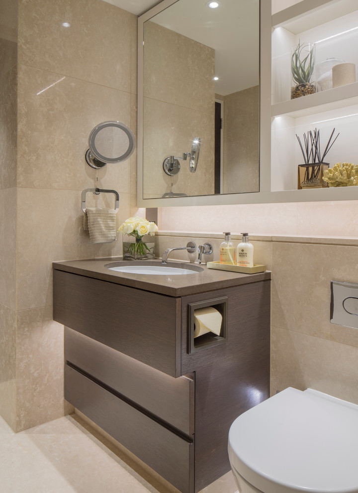 Cette image montre une salle de bain design avec un placard à porte plane, des portes de placard marrons, WC à poser, un carrelage beige et un lavabo encastré.