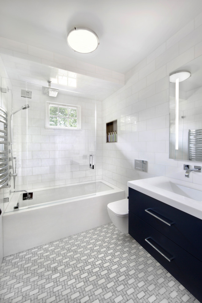 Стильный дизайн: ванная комната среднего размера в стиле модернизм с плоскими фасадами, синими фасадами, полновстраиваемой ванной, душем над ванной, инсталляцией, белой плиткой, мраморной плиткой, белыми стенами, полом из мозаичной плитки, врезной раковиной, мраморной столешницей, серым полом, душем с распашными дверями и белой столешницей - последний тренд