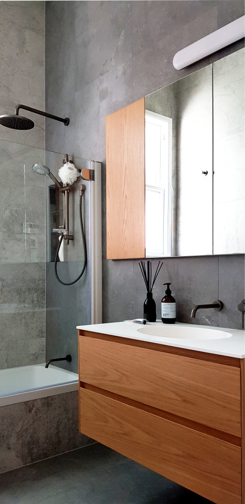 Idée de décoration pour une salle de bain design en bois brun avec un placard à porte plane, une baignoire en alcôve, un combiné douche/baignoire, un carrelage gris, un lavabo intégré, un sol gris et un plan de toilette blanc.