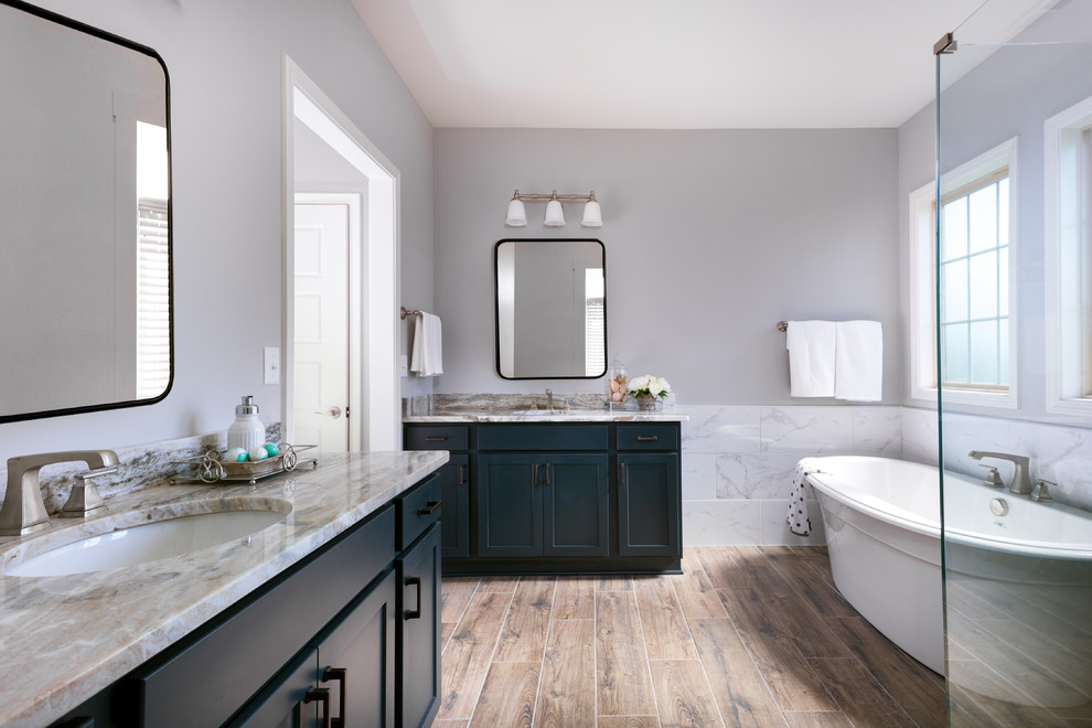 Elegant white tile medium tone wood floor and brown floor freestanding bathtub photo in Other with shaker cabinets, blue cabinets, gray walls, an undermount sink and beige countertops
