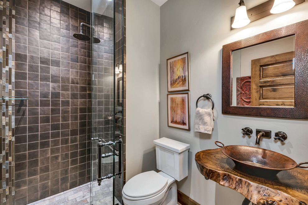Idéer för att renovera ett litet rustikt brun brunt badrum med dusch, med öppna hyllor, bruna skåp, en kantlös dusch, en toalettstol med hel cisternkåpa, brun kakel, kakel i metall, grå väggar, klinkergolv i porslin, ett fristående handfat, träbänkskiva, flerfärgat golv och med dusch som är öppen