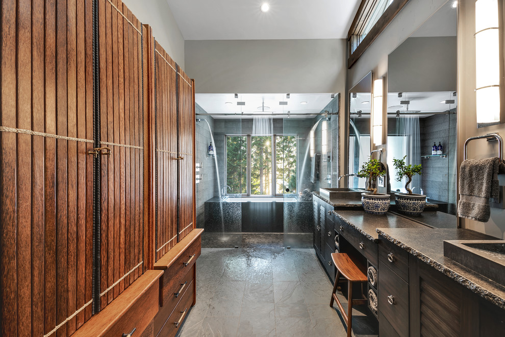 Example of a large mountain style master gray tile and stone tile ceramic tile and gray floor bathroom design in Other with brown cabinets, an undermount tub, a one-piece toilet, gray walls, a vessel sink, granite countertops, gray countertops and louvered cabinets
