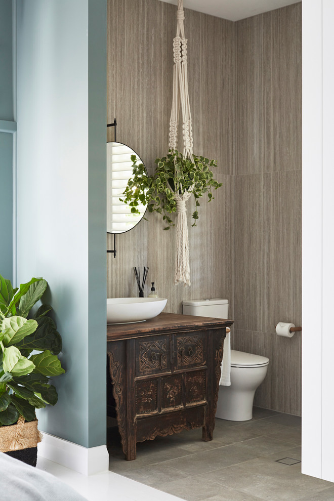 Foto på ett mellanstort tropiskt brun badrum med dusch, med skåp i mörkt trä, en toalettstol med hel cisternkåpa, grå kakel, porslinskakel, klinkergolv i porslin, ett fristående handfat, grått golv, grå väggar och träbänkskiva