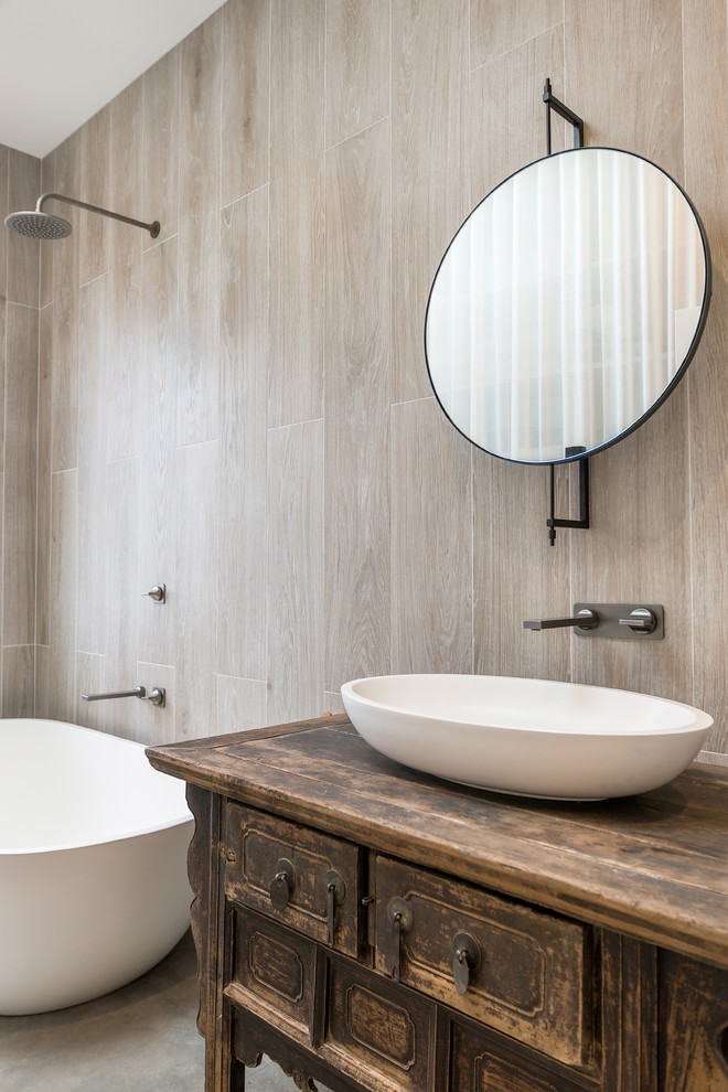 Foto på ett funkis brun badrum med dusch, med skåp i slitet trä, ett fristående badkar, en dusch/badkar-kombination, beige kakel, beige väggar, ett fristående handfat, träbänkskiva, grått golv, med dusch som är öppen och luckor med infälld panel