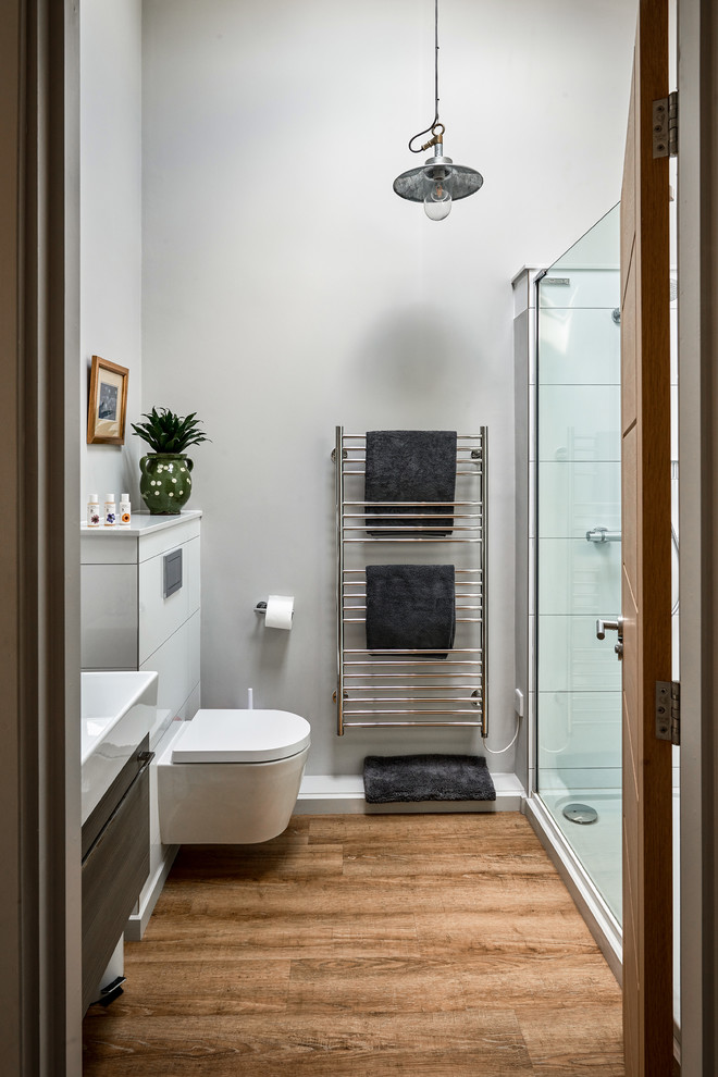Cette image montre une petite salle de bain principale rustique avec un placard à porte plane, des portes de placard grises, une douche d'angle, WC suspendus, un mur gris, un plan vasque, un sol marron et une cabine de douche à porte battante.