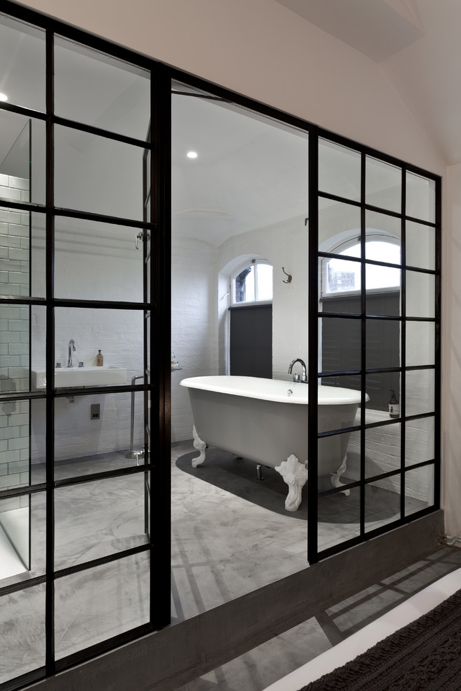 Immagine di una stanza da bagno contemporanea con vasca con piedi a zampa di leone, lavabo sospeso, pareti bianche e pavimento in cemento