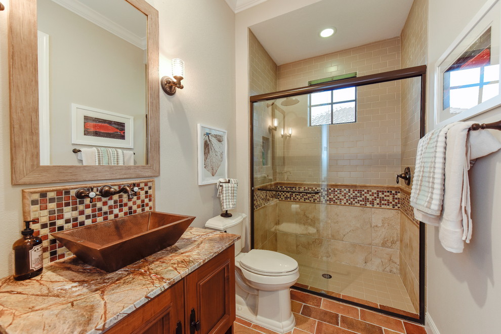 Example of a country multicolored tile and subway tile terra-cotta tile alcove shower design in Tampa with a vessel sink, raised-panel cabinets, medium tone wood cabinets, granite countertops, a two-piece toilet and gray walls