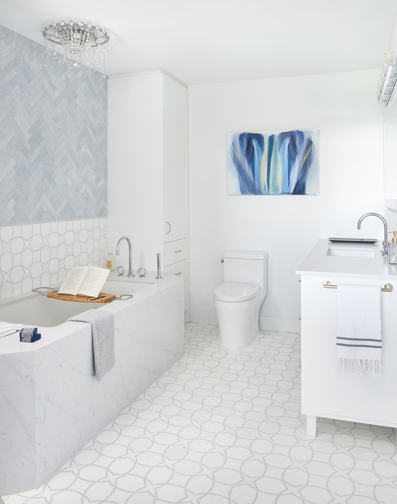 На фото: большая главная ванная комната в стиле модернизм с плоскими фасадами, белыми фасадами, полновстраиваемой ванной, унитазом-моноблоком, синей плиткой, мраморной плиткой, белыми стенами, мраморным полом, врезной раковиной, столешницей из искусственного кварца, белым полом и белой столешницей с