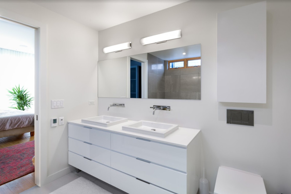 Cette image montre une salle de bain principale minimaliste de taille moyenne avec un placard à porte plane, des portes de placard blanches, une baignoire en alcôve, une douche d'angle, WC à poser, un carrelage gris, un mur blanc, un sol en galet, une vasque, un sol blanc, une cabine de douche à porte battante et un plan de toilette blanc.