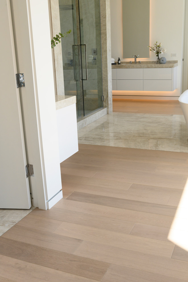 Expansive modern ensuite bathroom in Los Angeles with flat-panel cabinets, white cabinets, a claw-foot bath, a double shower, beige tiles, white walls, medium hardwood flooring, marble worktops, brown floors, a sliding door, beige worktops, a shower bench, double sinks and a built in vanity unit.