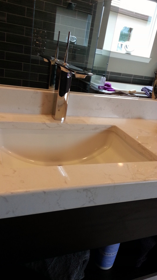 Réalisation d'une salle de bain design en bois foncé avec un lavabo encastré et un plan de toilette en quartz modifié.