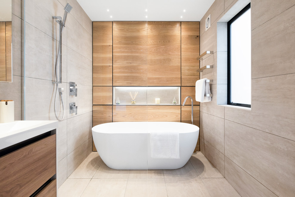 Modern inredning av ett badrum, med släta luckor, skåp i mellenmörkt trä, ett fristående badkar, våtrum, grå kakel, beiget golv och med dusch som är öppen