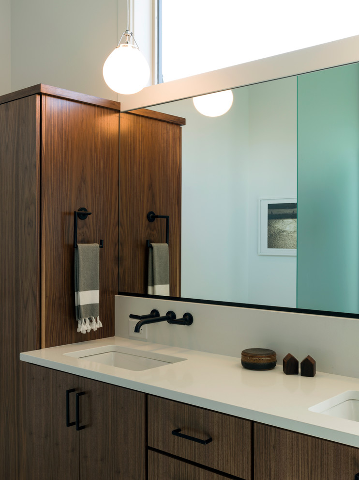 Immagine di una stanza da bagno padronale minimal con lavabo sottopiano, ante lisce, ante in legno bruno, top in superficie solida e pareti bianche