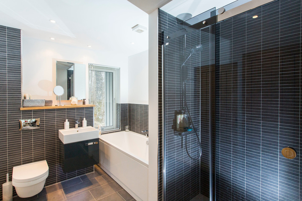 Exempel på ett mellanstort modernt vit vitt en-suite badrum, med släta luckor, grå skåp, ett hörnbadkar, en dusch i en alkov, en vägghängd toalettstol, vita väggar, träbänkskiva, grått golv, dusch med skjutdörr, stickkakel, svart kakel och ett integrerad handfat