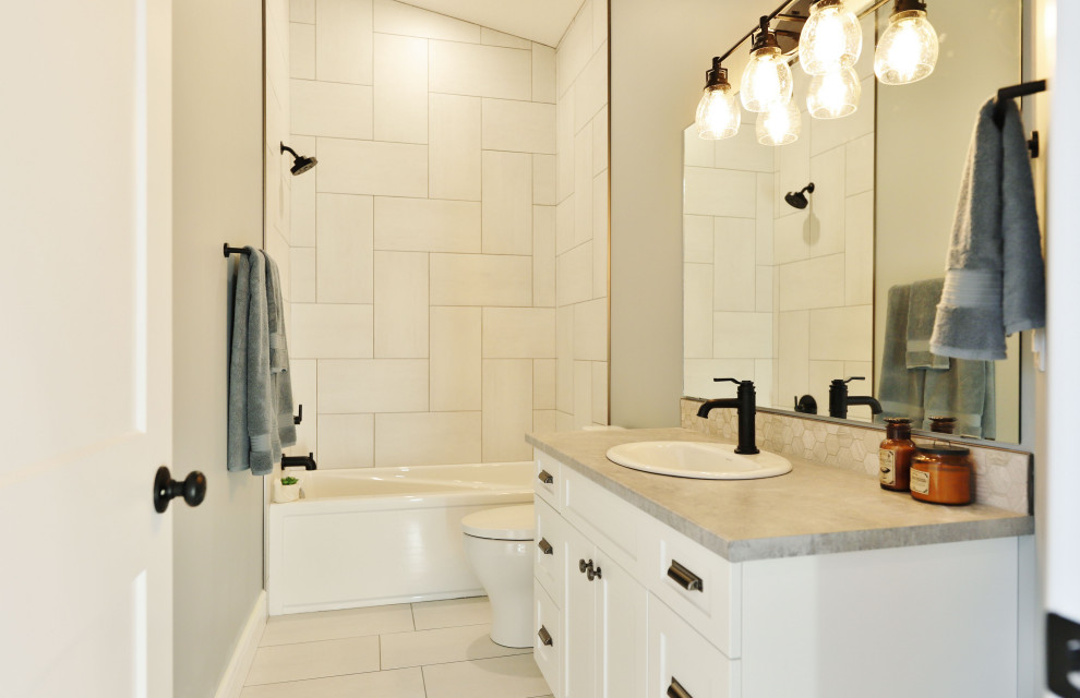 Bild på ett mellanstort lantligt grå grått badrum för barn, med skåp i shakerstil, vita skåp, ett badkar i en alkov, en dusch/badkar-kombination, vit kakel, keramikplattor, klinkergolv i keramik, ett nedsänkt handfat, laminatbänkskiva och vitt golv