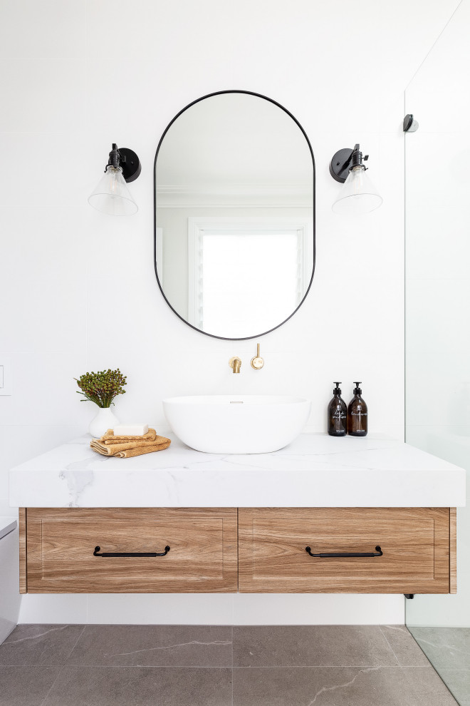 Свежая идея для дизайна: ванная комната среднего размера в морском стиле с фасадами в стиле шейкер, светлыми деревянными фасадами, открытым душем, унитазом-моноблоком, белой плиткой, керамогранитной плиткой, белыми стенами, полом из керамогранита, душевой кабиной, настольной раковиной, мраморной столешницей, серым полом, открытым душем, белой столешницей, тумбой под одну раковину и подвесной тумбой - отличное фото интерьера