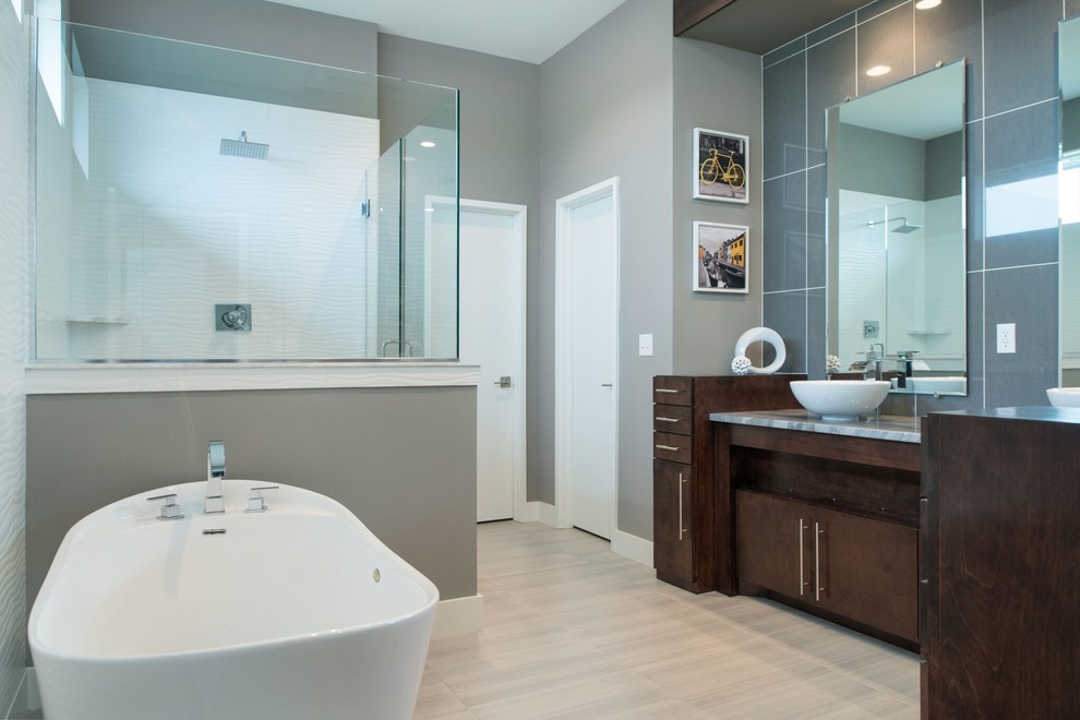 Inspiration for a large modern ensuite bathroom in Kansas City with flat-panel cabinets, dark wood cabinets, a freestanding bath, a corner shower, a two-piece toilet, blue tiles, grey tiles, glass tiles, grey walls, laminate floors, a vessel sink, granite worktops, beige floors and a hinged door.