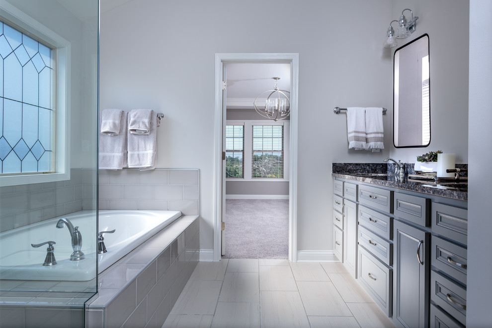 Foto di una stanza da bagno classica con ante con riquadro incassato, ante bianche, vasca da incasso, piastrelle beige, pareti beige, lavabo sottopiano, pavimento beige e top nero