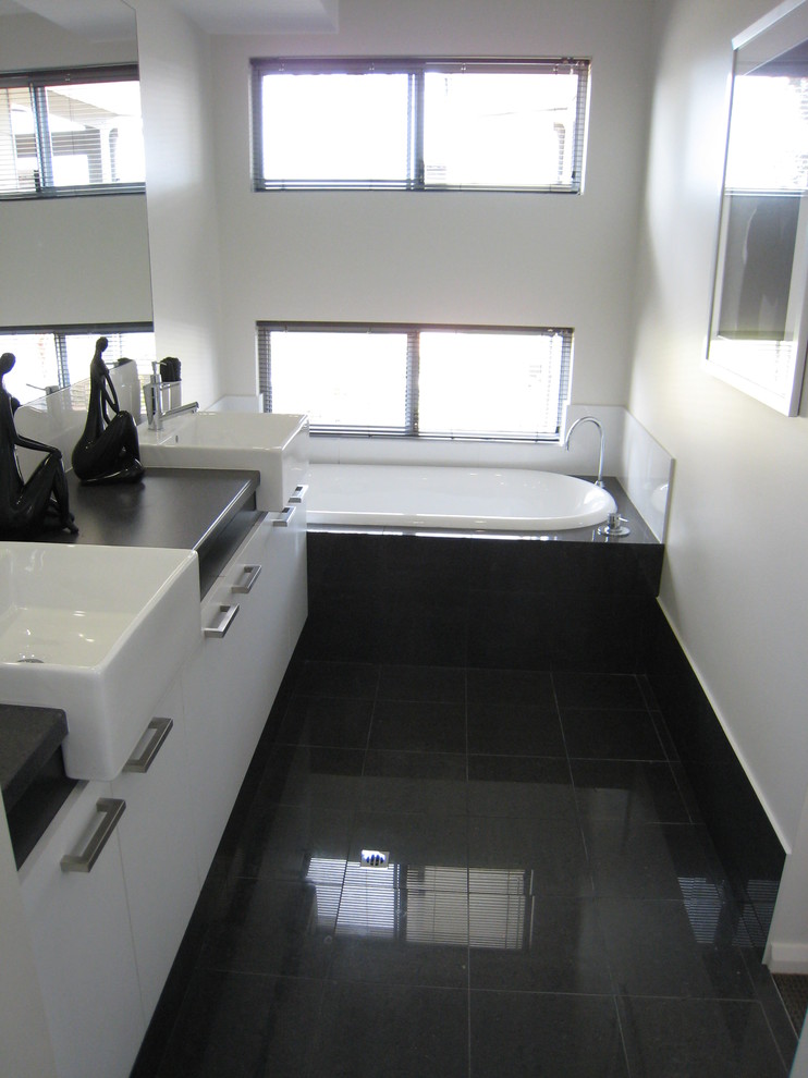 Bild på ett mellanstort funkis badrum för barn, med ett undermonterad handfat, släta luckor, vita skåp, laminatbänkskiva, ett platsbyggt badkar, grå kakel och vita väggar