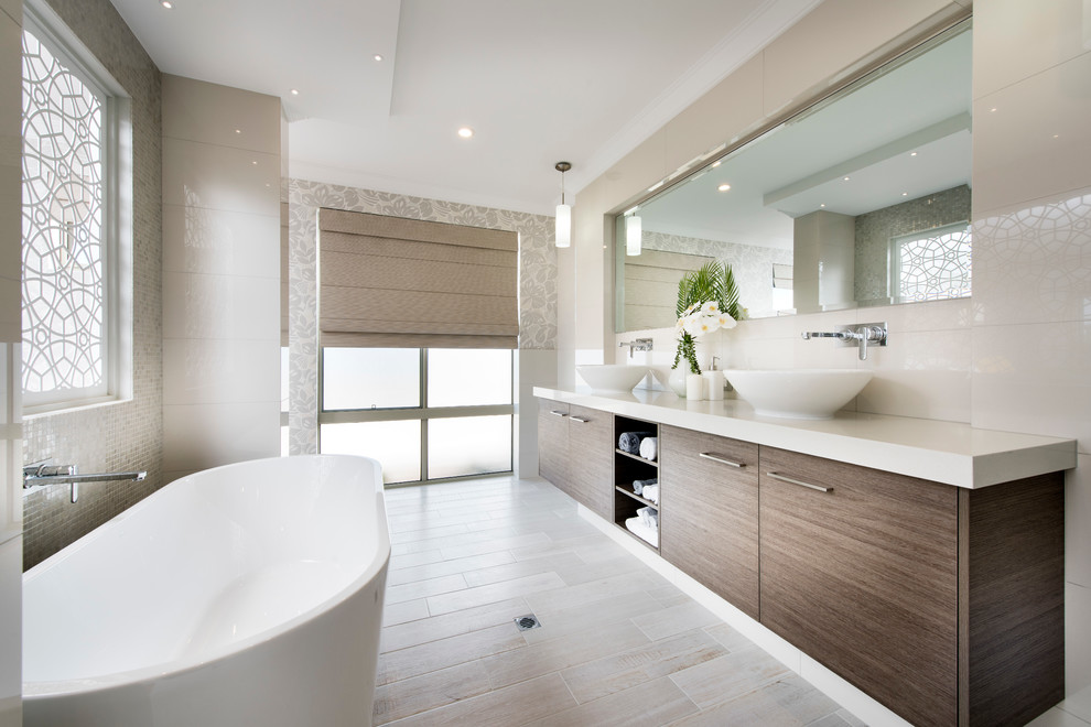 На фото: большая главная ванная комната в стиле модернизм с плоскими фасадами, фасадами цвета дерева среднего тона, отдельно стоящей ванной, бежевой плиткой, бежевыми стенами и настольной раковиной с