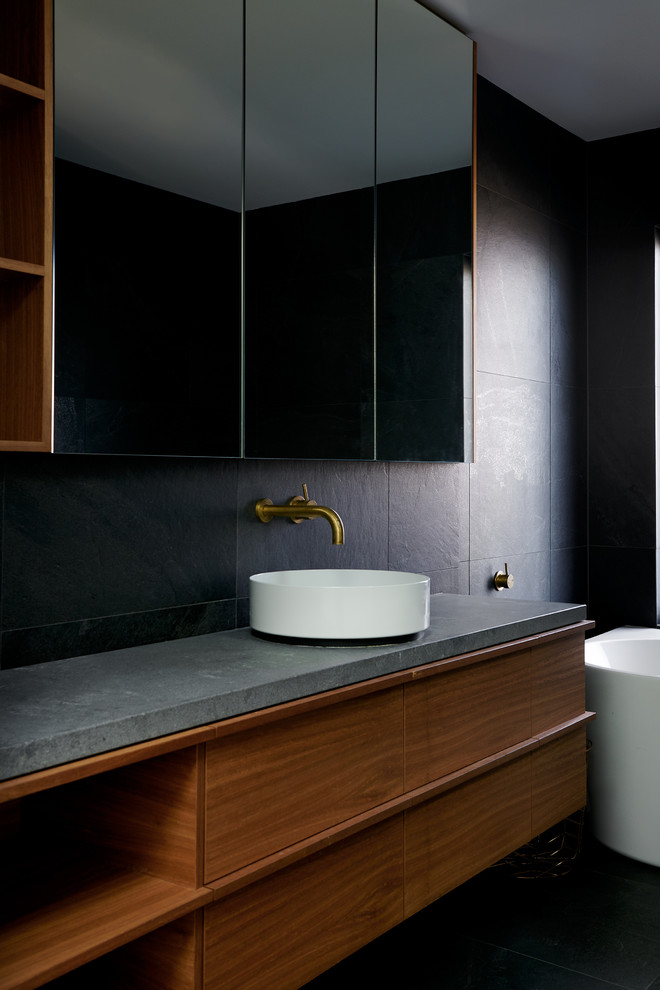 На фото: ванная комната в современном стиле с плоскими фасадами, фасадами цвета дерева среднего тона, черными стенами, настольной раковиной, столешницей из бетона, черным полом и серой столешницей с