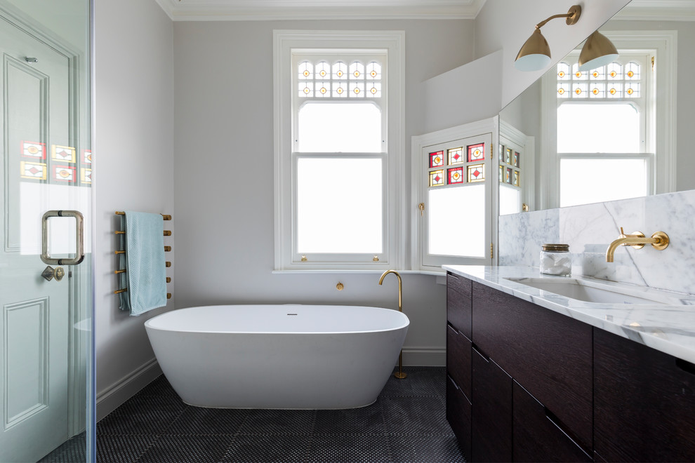 Design ideas for a contemporary ensuite bathroom in London with flat-panel cabinets, dark wood cabinets, a freestanding bath, grey walls, a submerged sink, marble worktops, black floors and white worktops.