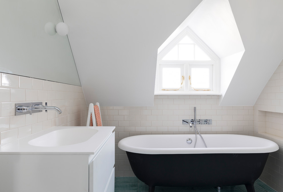 This is an example of a contemporary bathroom in London with flat-panel cabinets, white cabinets, a claw-foot bath, beige tiles, metro tiles, beige walls, an integrated sink, green floors and white worktops.