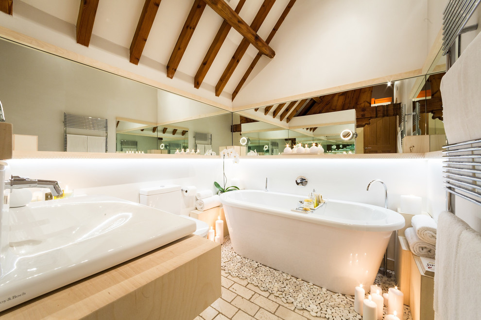 Diseño de cuarto de baño actual con lavabo encastrado, puertas de armario de madera clara, bañera exenta, paredes blancas y suelo de ladrillo