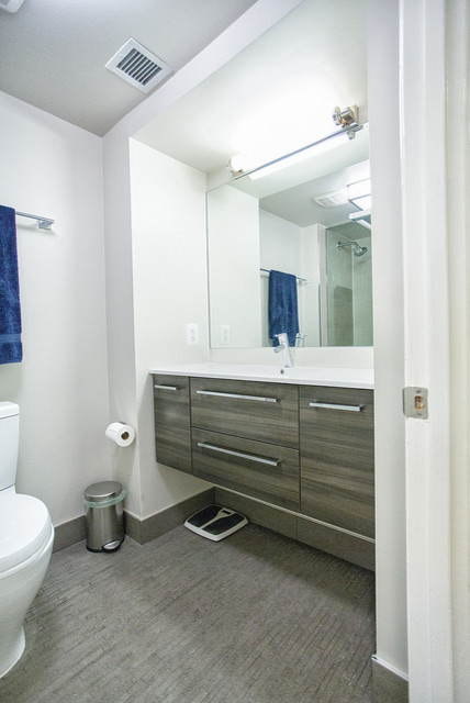 Cette photo montre une salle de bain moderne de taille moyenne avec un lavabo intégré, WC séparés, des carreaux de céramique, un mur blanc, un sol en carrelage de céramique, un placard à porte plane, des portes de placard grises, un plan de toilette en quartz modifié, une baignoire en alcôve, un combiné douche/baignoire et un carrelage gris.