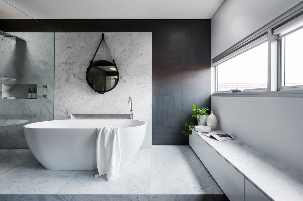 Cette image montre une grande salle de bain principale design avec une baignoire indépendante, une douche ouverte, un carrelage gris, des dalles de pierre, un mur gris, un sol en marbre et un plan de toilette en surface solide.