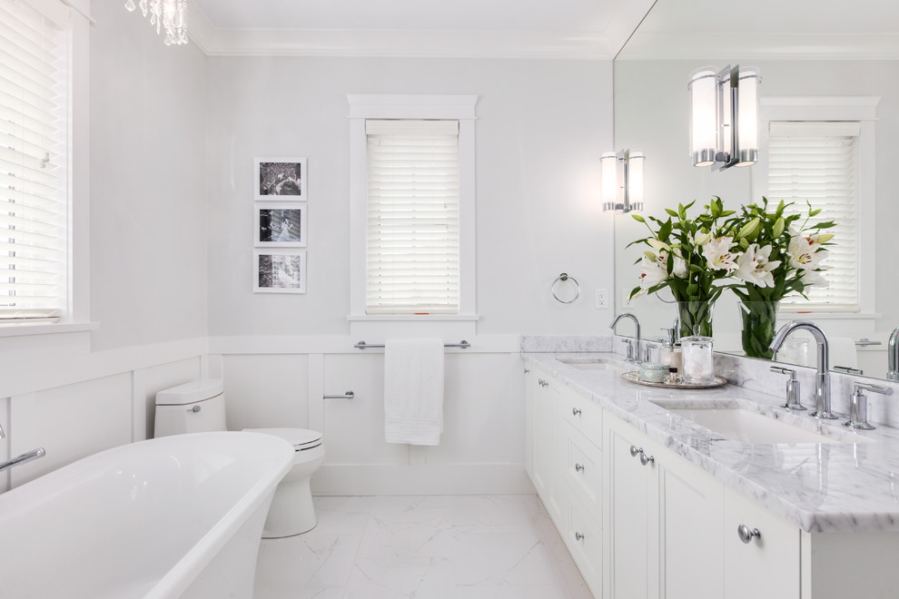 Medium sized traditional ensuite bathroom in Vancouver with a submerged sink, white cabinets, marble worktops, a freestanding bath, a corner shower, a one-piece toilet, white tiles, porcelain tiles, grey walls, marble flooring and recessed-panel cabinets.