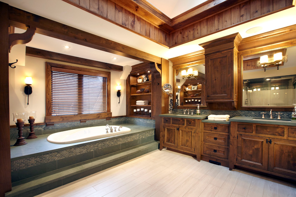 Cette photo montre une grande salle de bain principale montagne en bois brun avec un placard avec porte à panneau encastré, une baignoire posée, un carrelage vert, des carreaux en allumettes, un mur beige, un sol en carrelage de céramique et un lavabo encastré.
