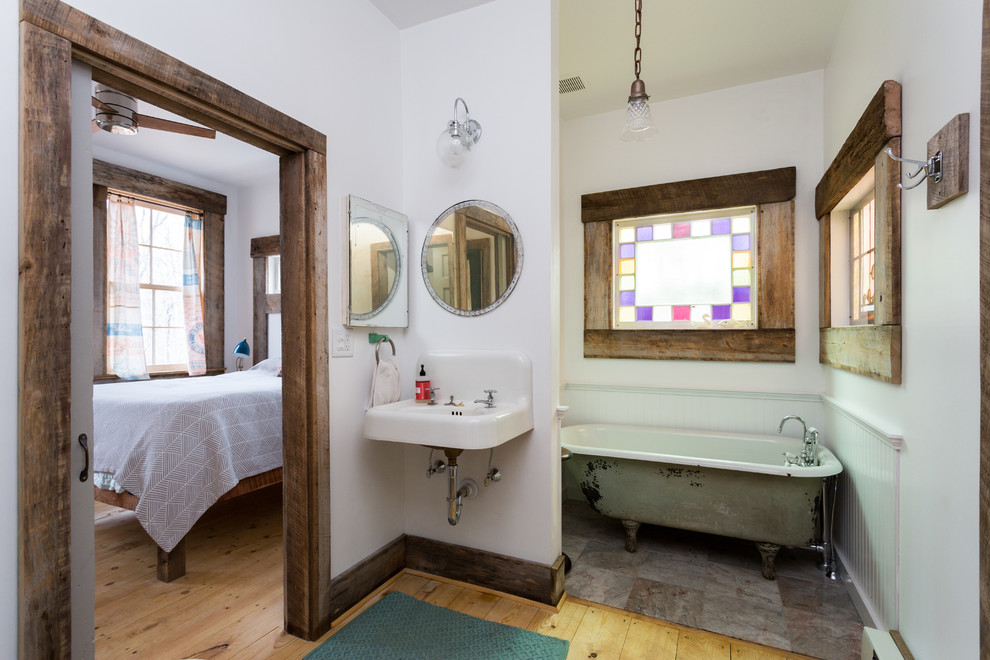 Bild på ett litet lantligt en-suite badrum, med ett badkar med tassar, en toalettstol med separat cisternkåpa, flerfärgad kakel, stenkakel, vita väggar, ljust trägolv och ett väggmonterat handfat
