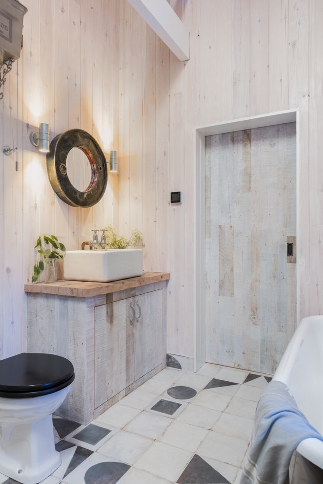 На фото: ванная комната в деревянном доме в стиле рустика с светлыми деревянными фасадами, отдельно стоящей ванной, раздельным унитазом, бежевыми стенами, полом из керамической плитки, настольной раковиной, столешницей из дерева, разноцветным полом, плоскими фасадами, душевой кабиной и коричневой столешницей с