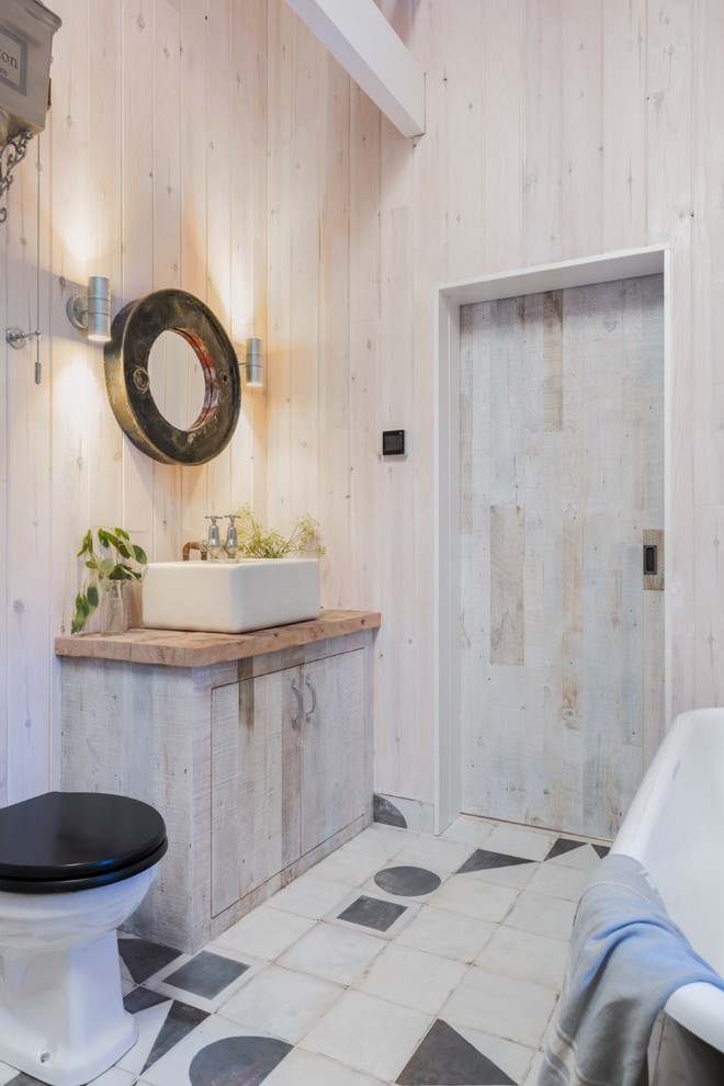 Inspiration for a rustic 3/4 ceramic tile and multicolored floor freestanding bathtub remodel in Cornwall with light wood cabinets, a two-piece toilet, beige walls, a vessel sink, wood countertops, flat-panel cabinets and brown countertops