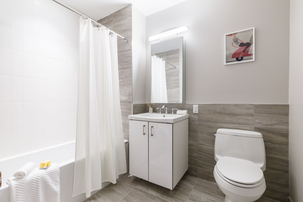 Cette image montre une salle d'eau design de taille moyenne avec un placard à porte plane, des portes de placard blanches, une baignoire en alcôve, un combiné douche/baignoire, WC à poser, un carrelage gris, des carreaux de porcelaine, un mur gris, un sol en carrelage de porcelaine, un lavabo intégré, un sol gris, une cabine de douche avec un rideau, un plan de toilette blanc et meuble-lavabo encastré.