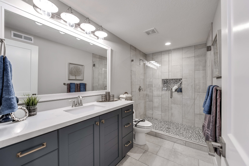 Cette photo montre une salle de bain chic de taille moyenne avec un placard à porte shaker, des portes de placard grises, un carrelage gris, des carreaux de porcelaine, un mur gris, un sol en carrelage de porcelaine, un lavabo encastré et un plan de toilette en surface solide.