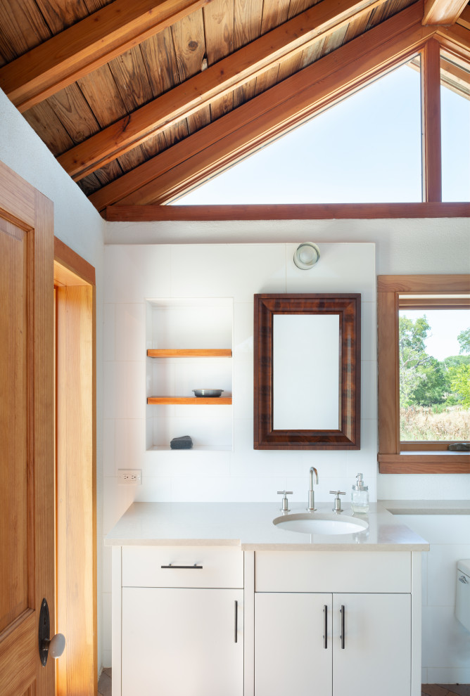 Small farmhouse ensuite bathroom in Austin with dark wood cabinets, a one-piece toilet, white tiles, metro tiles, white walls, brick flooring, a submerged sink, solid surface worktops, red floors, a hinged door, grey worktops, a single sink, a built in vanity unit and exposed beams.