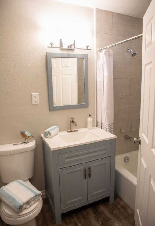 Источник вдохновения для домашнего уюта: маленькая ванная комната в стиле кантри с фасадами с выступающей филенкой, серыми фасадами, душем в нише, унитазом-моноблоком, белой плиткой, керамической плиткой, серыми стенами, полом из цементной плитки, монолитной раковиной, столешницей из искусственного кварца, черным полом, душем с распашными дверями и белой столешницей для на участке и в саду