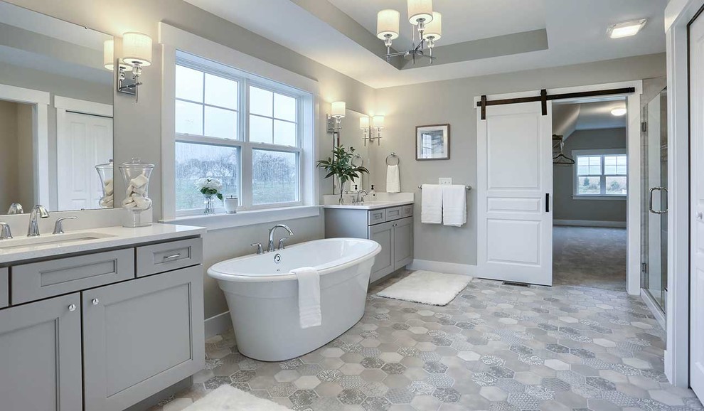 На фото: большая главная ванная комната в стиле кантри с серыми фасадами, отдельно стоящей ванной, душем в нише, унитазом-моноблоком, серыми стенами, полом из керамической плитки, врезной раковиной, мраморной столешницей, душем с распашными дверями, белой столешницей и серым полом