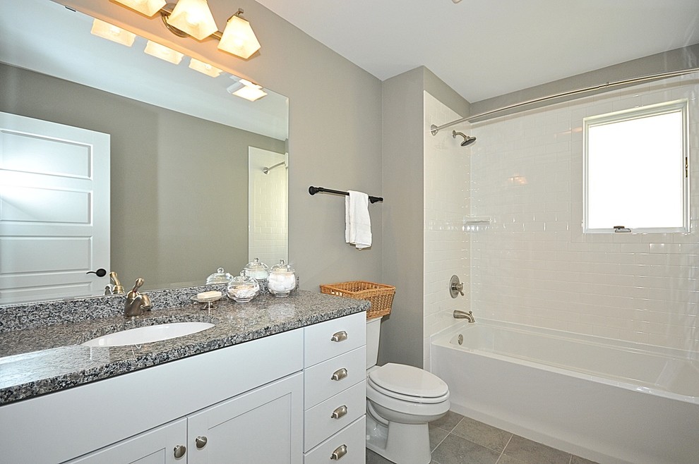 Aménagement d'une salle de bain classique avec des portes de placard blanches, un plan de toilette en granite, un carrelage blanc, un carrelage métro et un mur gris.