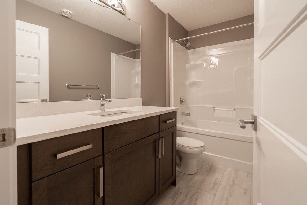 Cette image montre une salle de bain craftsman de taille moyenne avec des portes de placard marrons, une baignoire en alcôve, un combiné douche/baignoire, WC séparés, un carrelage blanc, des carreaux de céramique, un mur gris, un lavabo encastré, un plan de toilette en quartz, un sol gris, une cabine de douche avec un rideau et un plan de toilette blanc.